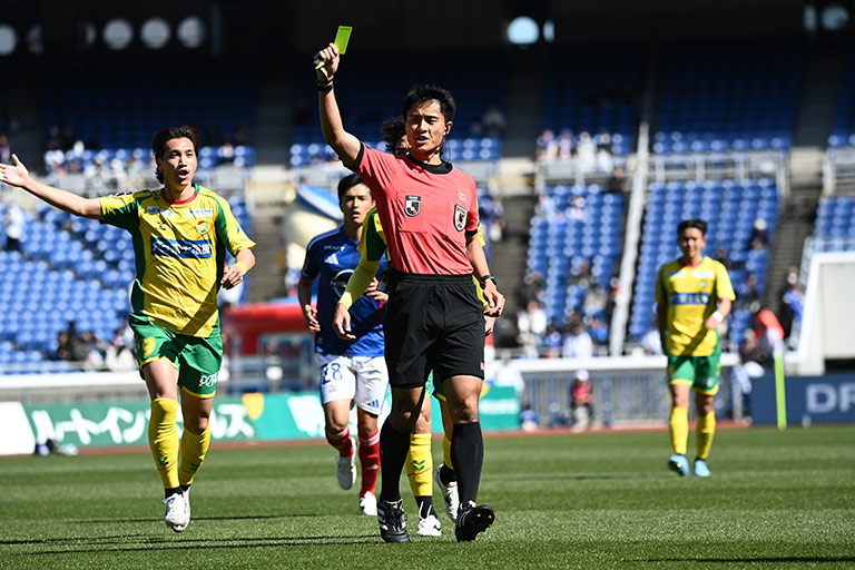 写真：イエローカードを上げる主審