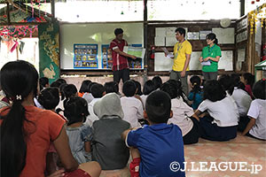 本田氏がカレン族のシャツを身にまとい子供たちに絵本の読み聞かせを行う