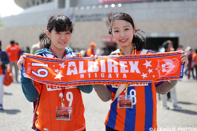 チームカラーのタオルマフラーを掲げて笑顔の新潟ファン・サポーター