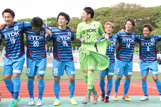 負傷交代した小澤 章人（#1）のユニフォームを掲げながら勝利を喜ぶ松本 拓也（#21）【明治安田Ｊ３ 第10節 秋田vs鹿児島】